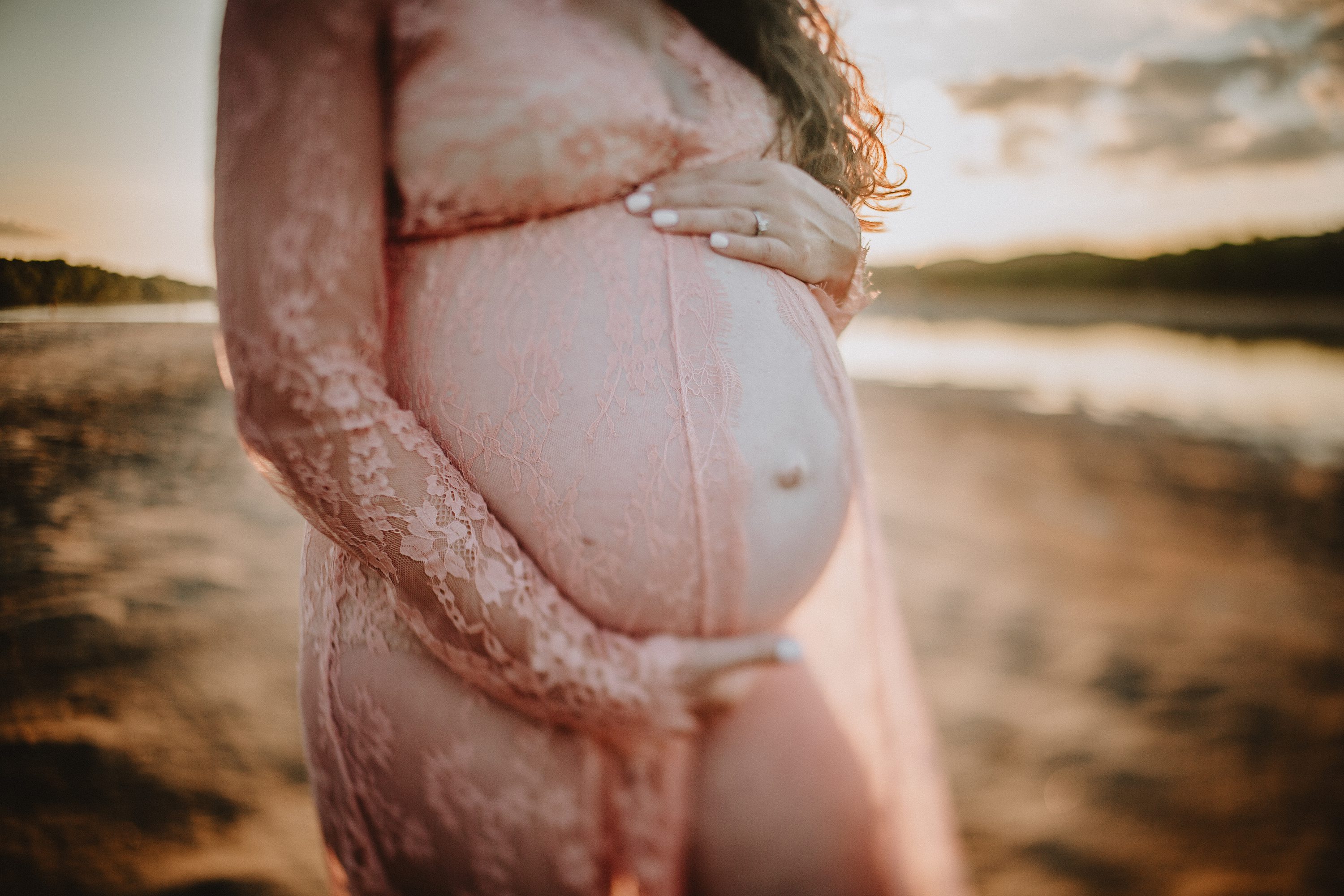 Maternity session by the river,Pregnant mother in a lace gown by the beach,PPregnant mother in a peach, lace gown by the water.,Pregnant mother in a long, lace gown holding her belly.,Pregnant woman in a peach gown near the river at sunset.