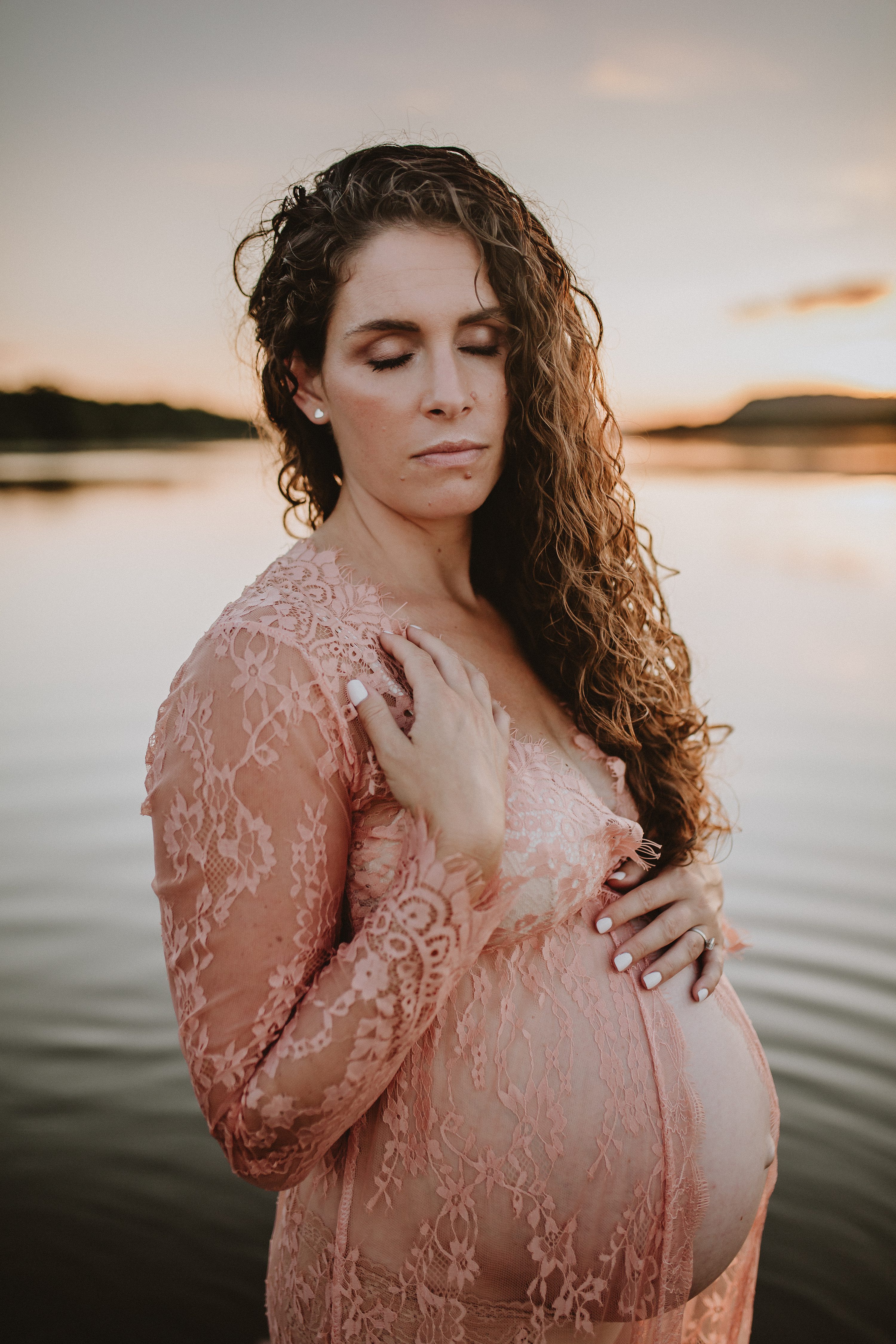 Maternity session by the river,Pregnant mother in a lace gown by the beach,PPregnant mother in a peach, lace gown by the water.,Pregnant mother in a long, lace gown holding her belly.,Pregnant woman in a peach gown near the river at sunset.