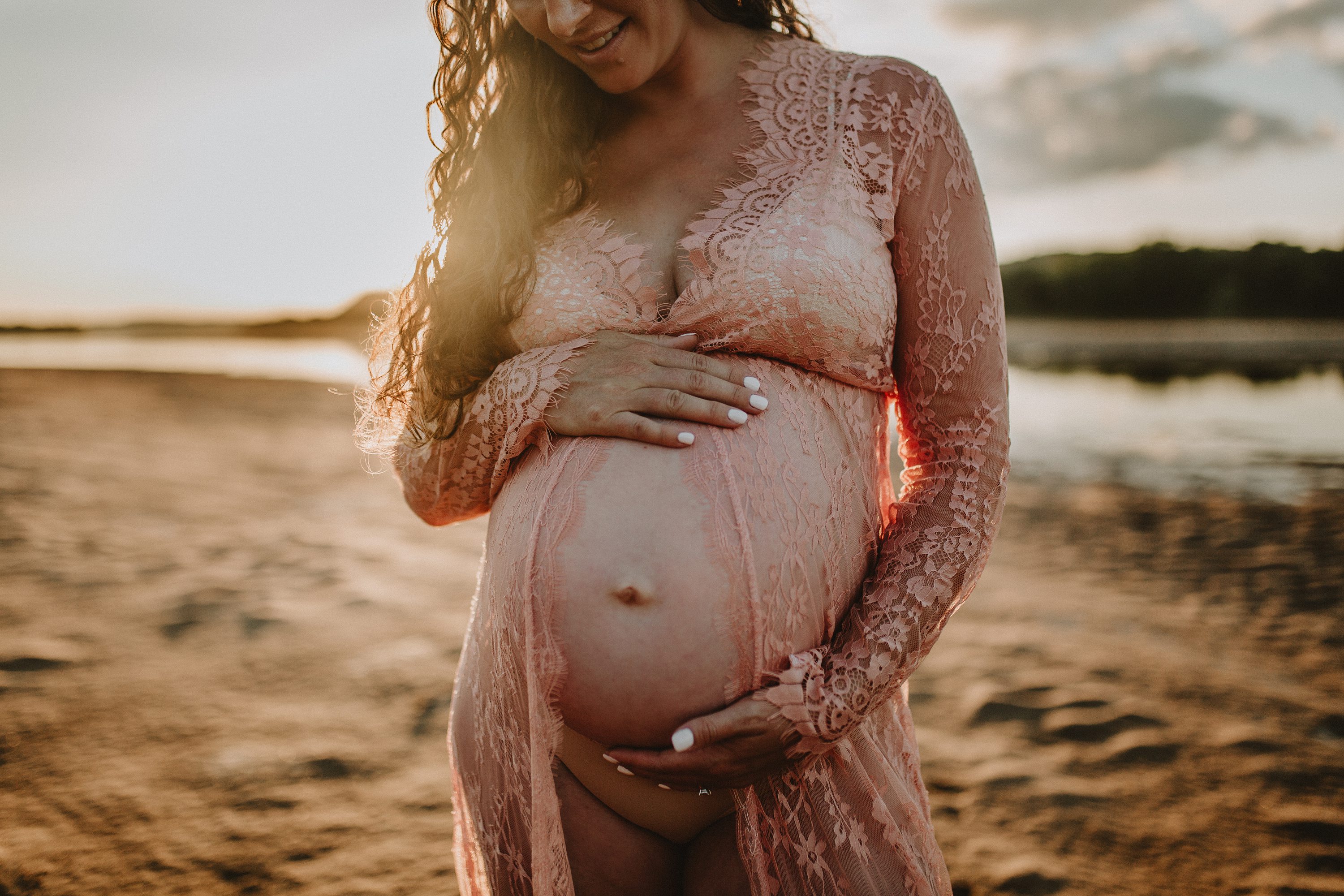 Maternity session by the river,Pregnant mother in a lace gown by the beach,PPregnant mother in a peach, lace gown by the water.,Pregnant mother in a long, lace gown holding her belly.,Pregnant woman in a peach gown near the river at sunset.